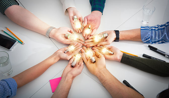 Several hands holding lit up lightbulbs