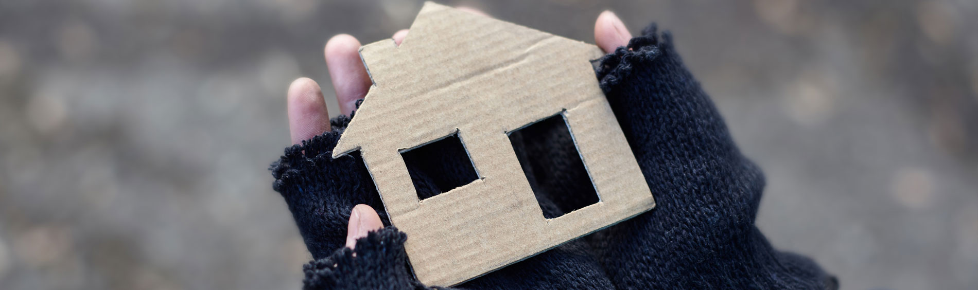 A homeless individual holds a cardboard cut out of a house