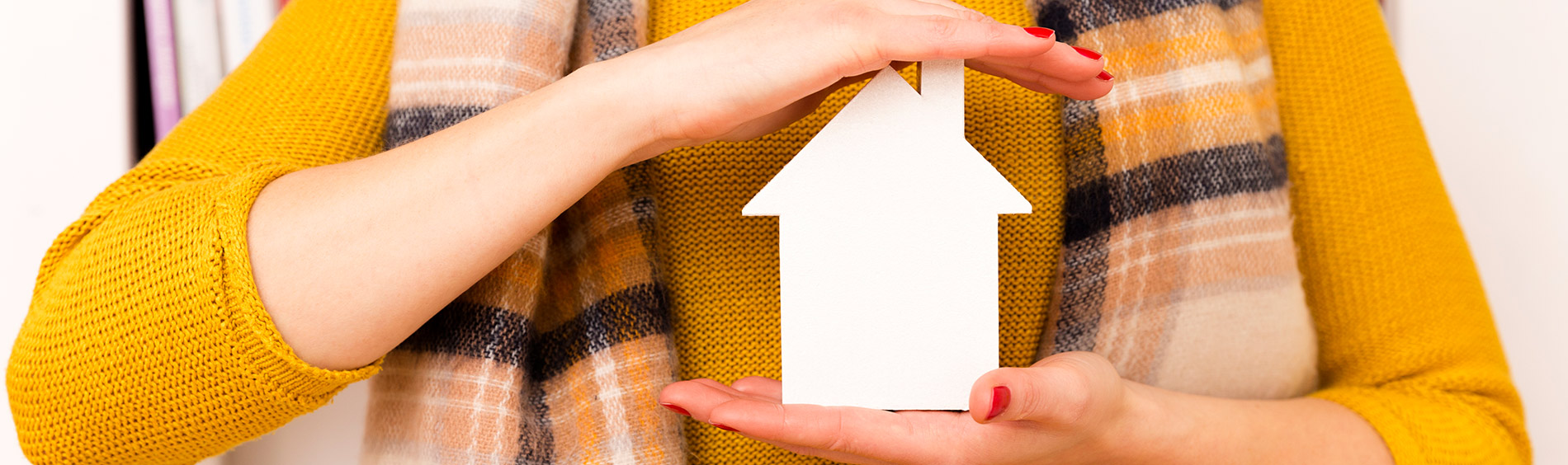 a woman holds a cardboard cut out of a house in her hands