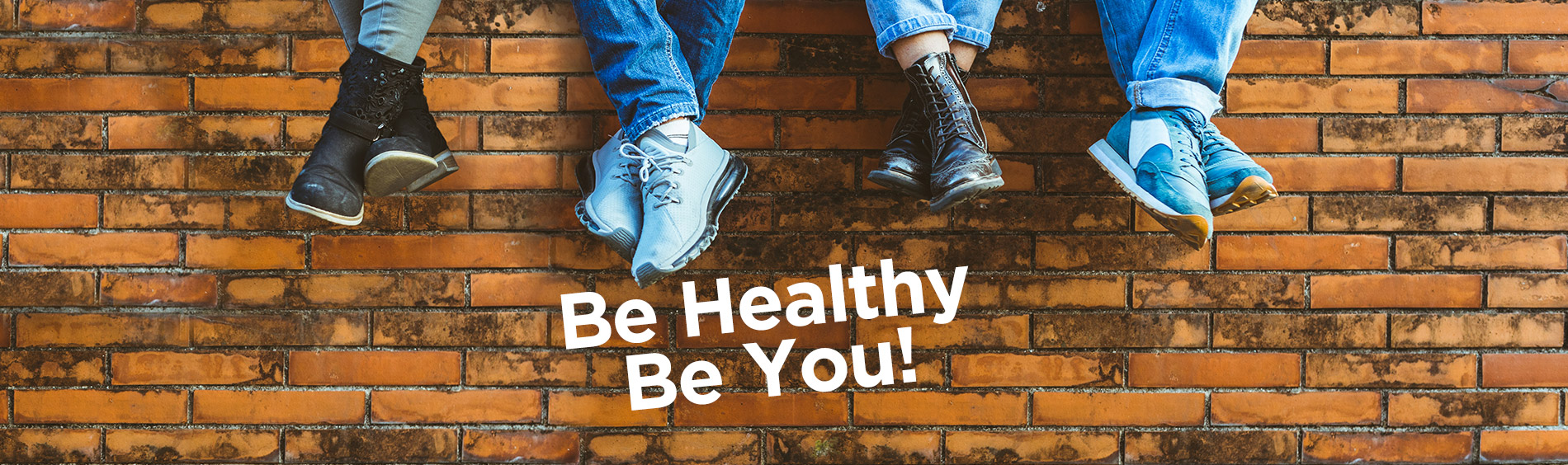 People sitting on a brick wall with the Be Healthy Be You Logo