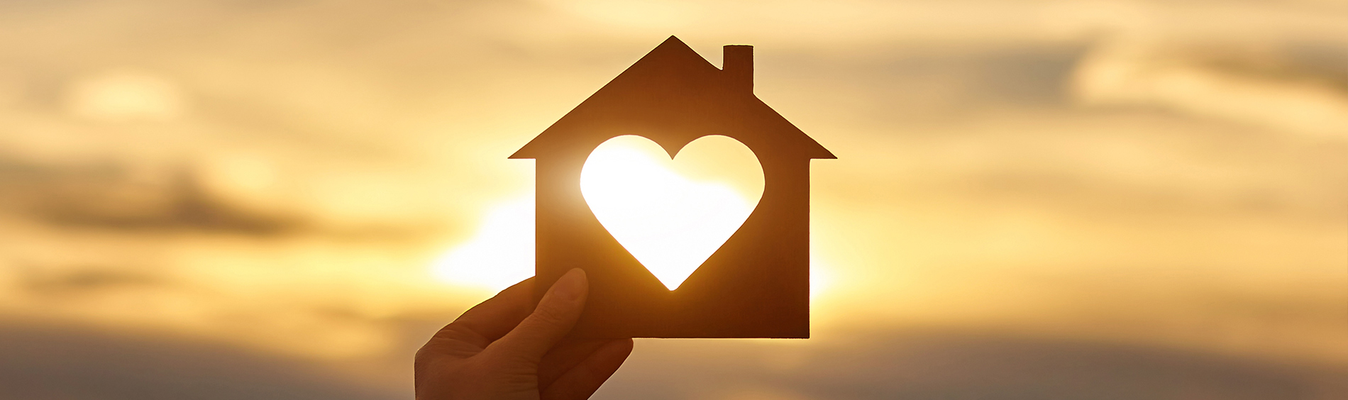 A paper cut out house being held up against a sunset by a hand