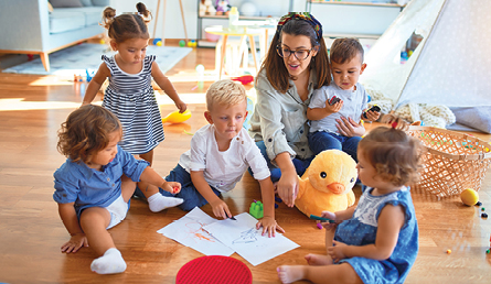 A childcare professional plays on the floor with a group of infant children