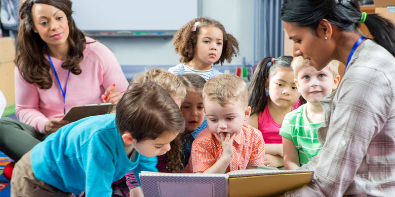 Group of children reading from a book held by teacher