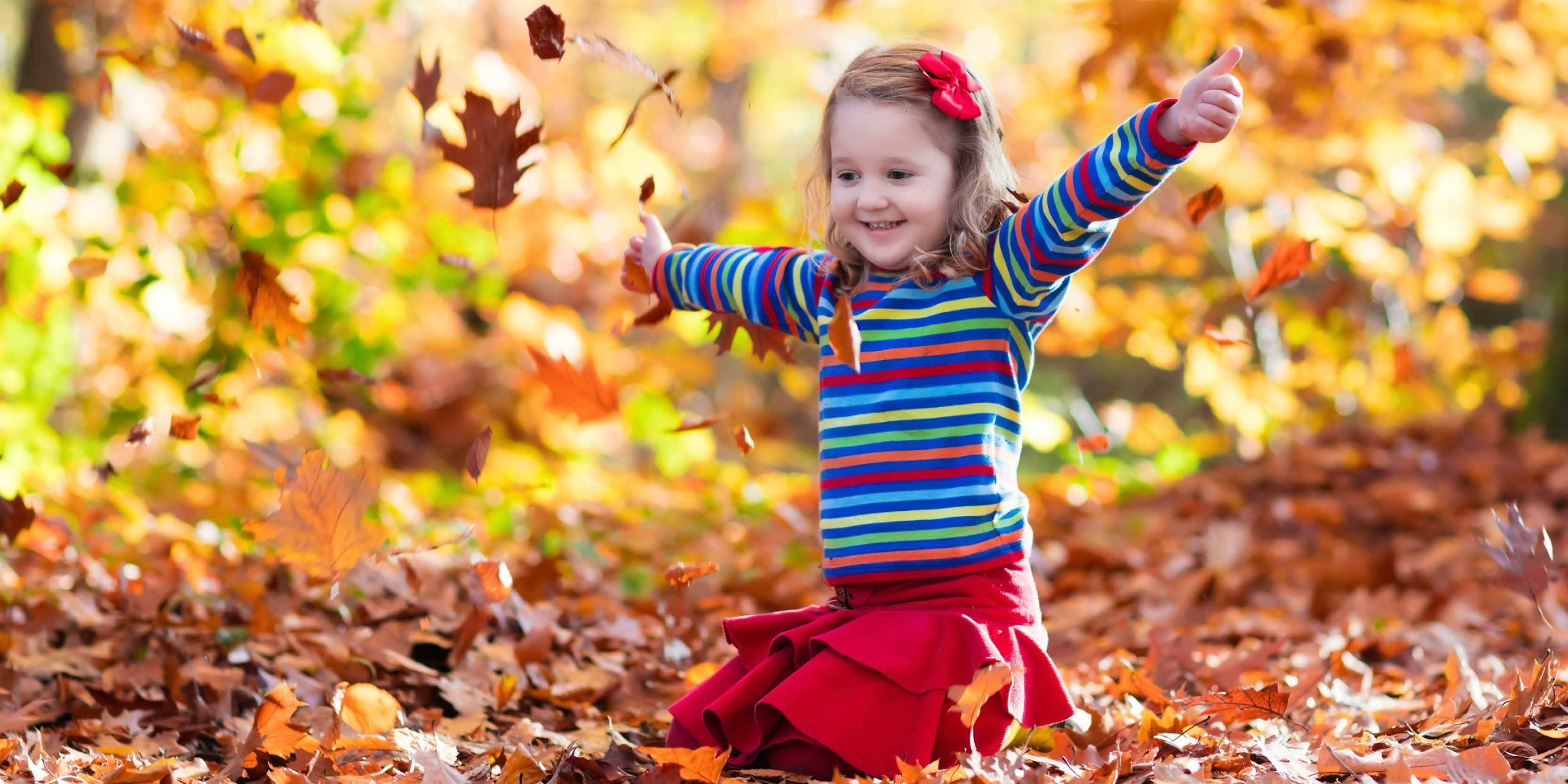 Little girl playing in colourful fall leaves