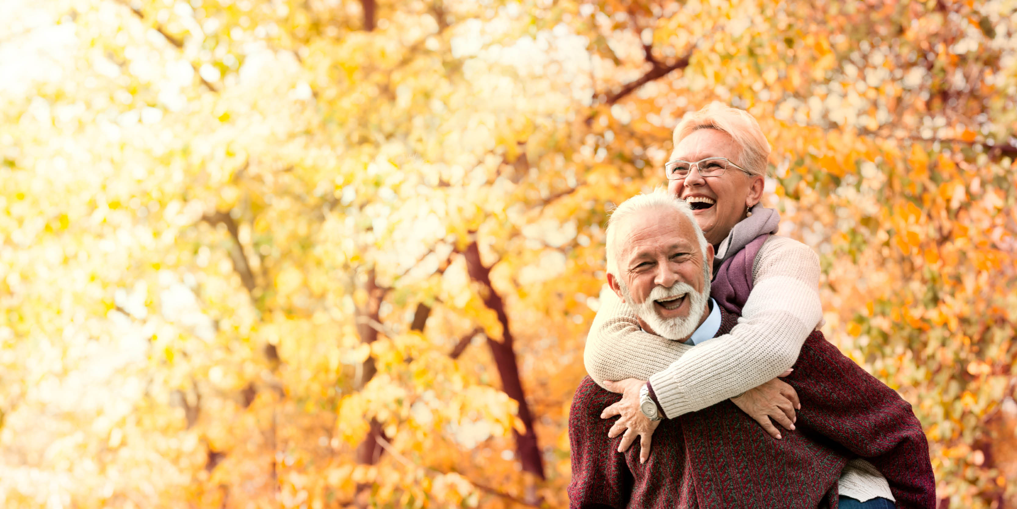 An older couple in front of fall trees