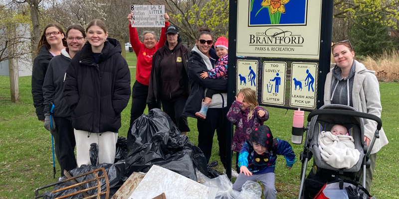 Members of the Brantford Station Neighbourhood Association participate in the Let’s Clean Our City community cleanup by posing for a photo with collected trash under the Edward Goold Park sign