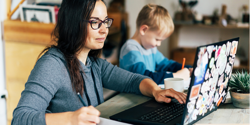 Mother at a computer studying with her child in the background