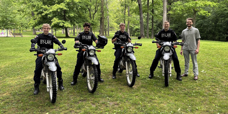Four City of Brantford Park Patrollers pose on motorcycles alongside their Supervisor in a park