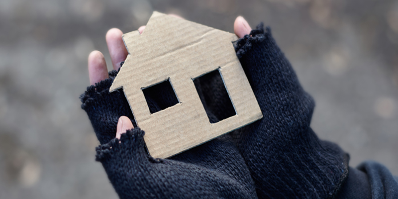 A pair of gloved hands holding a cardboard cut out of a house