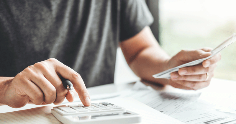 Someone typing into a calculator with papers on a desk