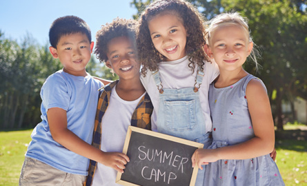 Four children holding up a chalkboard sign that reads Summer Camp