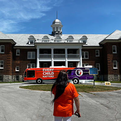 A woman wearing an orange shirt standing in front of the Woodland Cultural Centre