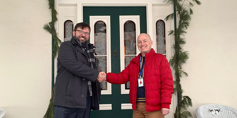 Two curators stand on the Bell Homestead NHS verandah shaking hands