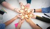 Several hands holding lit up lightbulbs