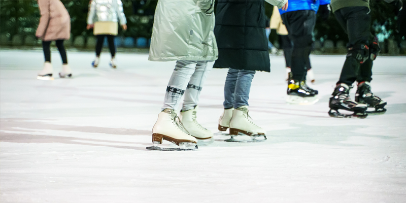 Up close photo of peoples skates on an outdoor ice rink at night